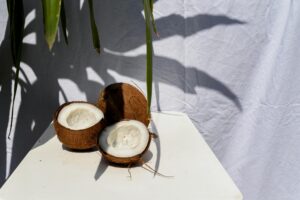 Halved coconuts on a table under natural sunlight with leaf shadows in a tropical setting.