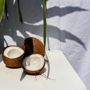 Halved coconuts on a table under natural sunlight with leaf shadows in a tropical setting.